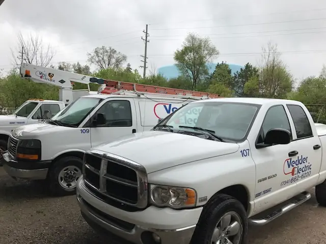 Three Vedder Electric vehicles, a bucket truck, a cargo van and a pickup, parked together with the company name and phone number on the doors